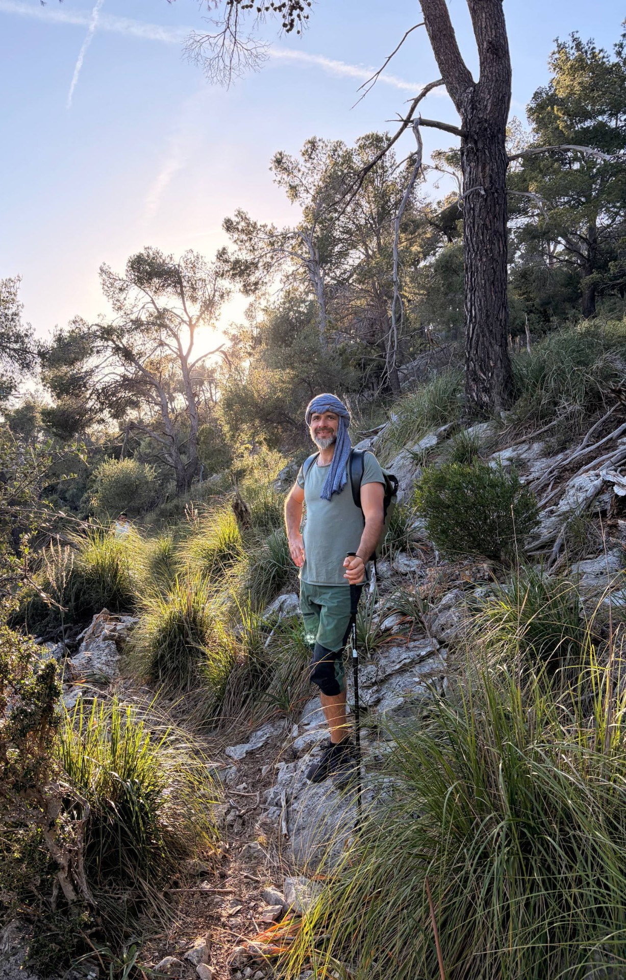 Damir Butkovic standing on a mountain trail with trekking poles, looking towards the camera